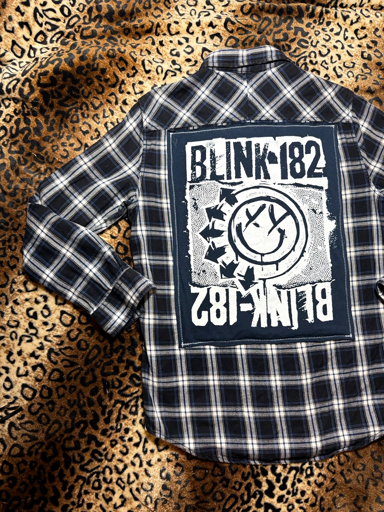 Plaid shirt with Blink-182 logo on a leopard print background
