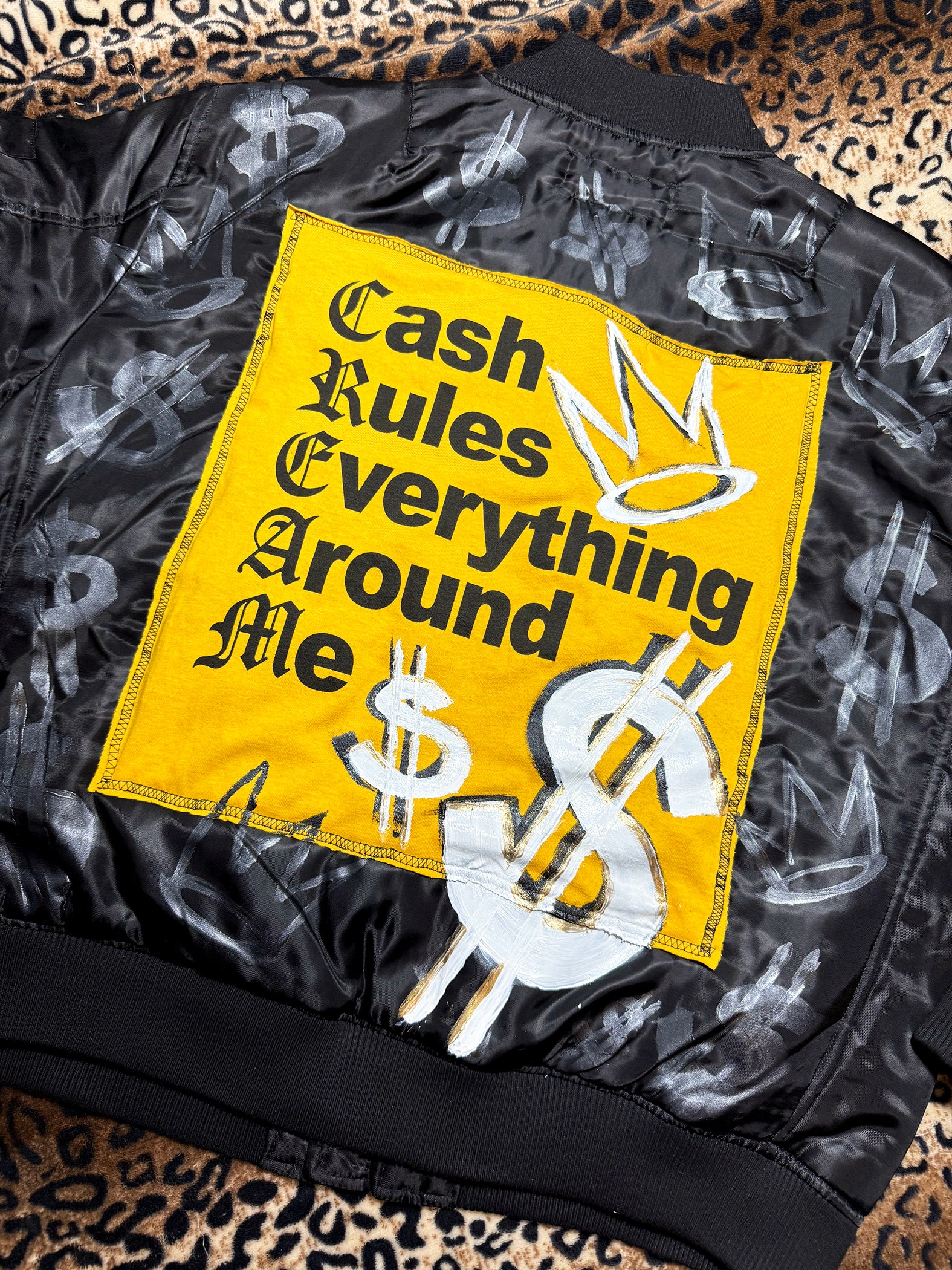 Black jacket with a yellow patch featuring text and dollar signs on a leopard print background