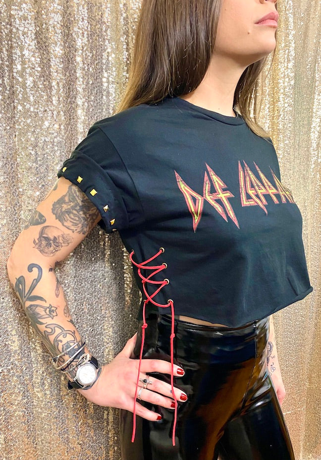 black def leppard crop top on tattooed model with black vinyl pants in front of gold background side view