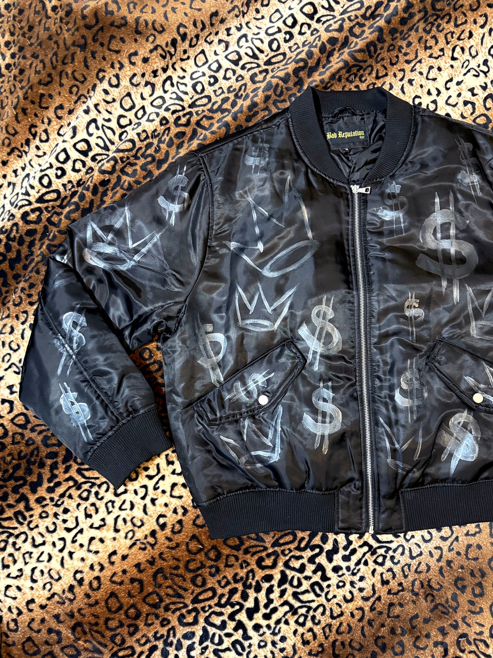 Black bomber jacket with silver graphics on a leopard print background