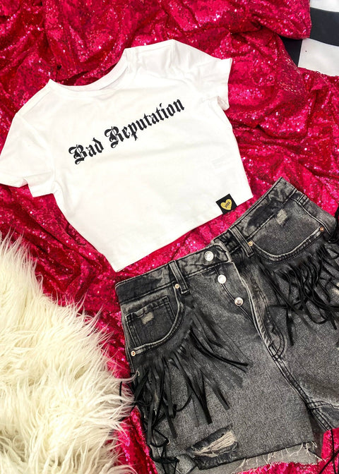 white "bad reputation" baby t on a hot pink sequin background with black denim shorts