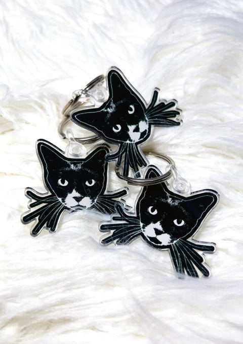 3 black cat face keychains on a white furry background