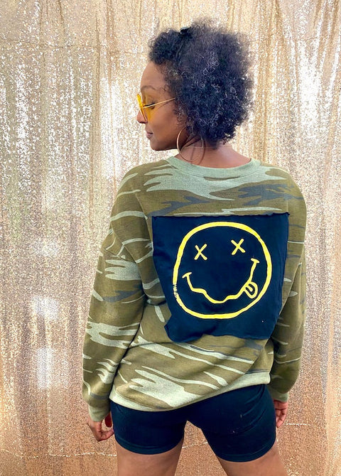 camo sweatshirt with nirvana logo back patch on front on model in front of gold background