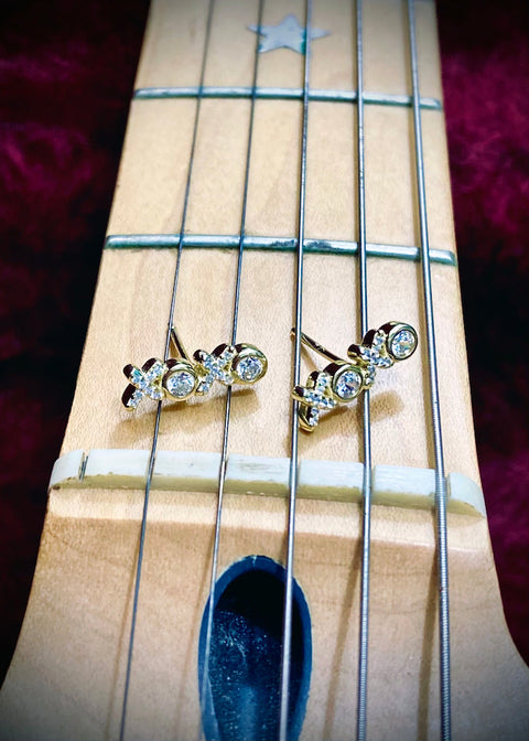 gold and faux diamond earrings in the shape of "xoxo" on the frets of a fender guitar