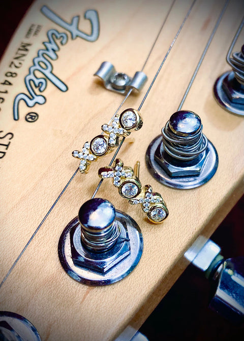 gold and faux diamond earrings in the shape of "xoxo" on the neck of a fender guitar